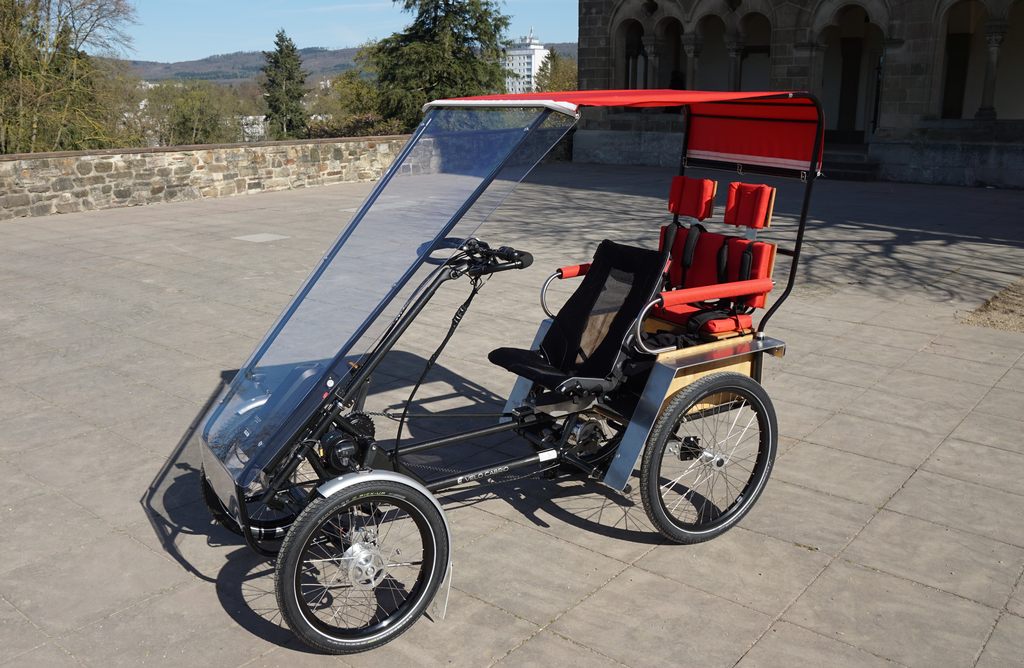 Quadricycle with retractable textile rooftop and full wind screen, two child seats in the back behind the driver