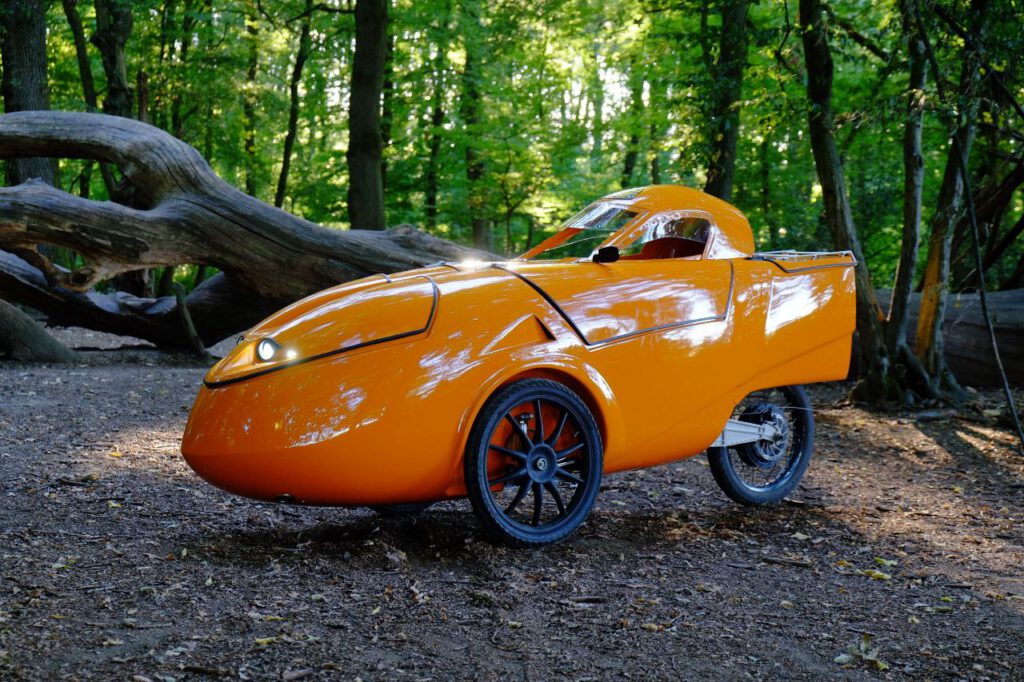 Velomobile with cargo capacity, fully enclosed recumbent, direct drive, recuperation, forest background